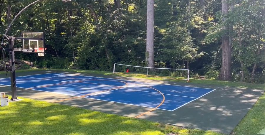 Multi-sport backyard court with a pickleball net and basketball hoop on one painted pad